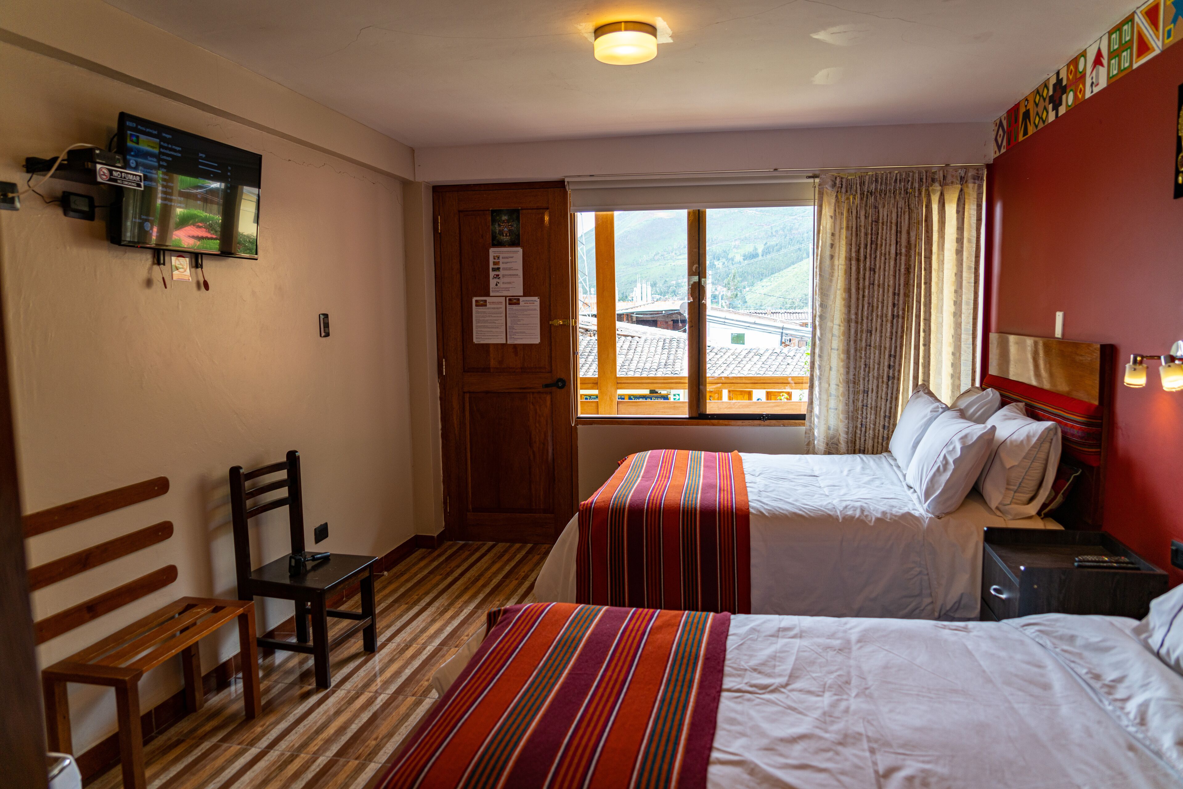 Une chambre d’hôtel avec deux lits, un banc en bois, un bureau et un téléviseur fixé au mur.