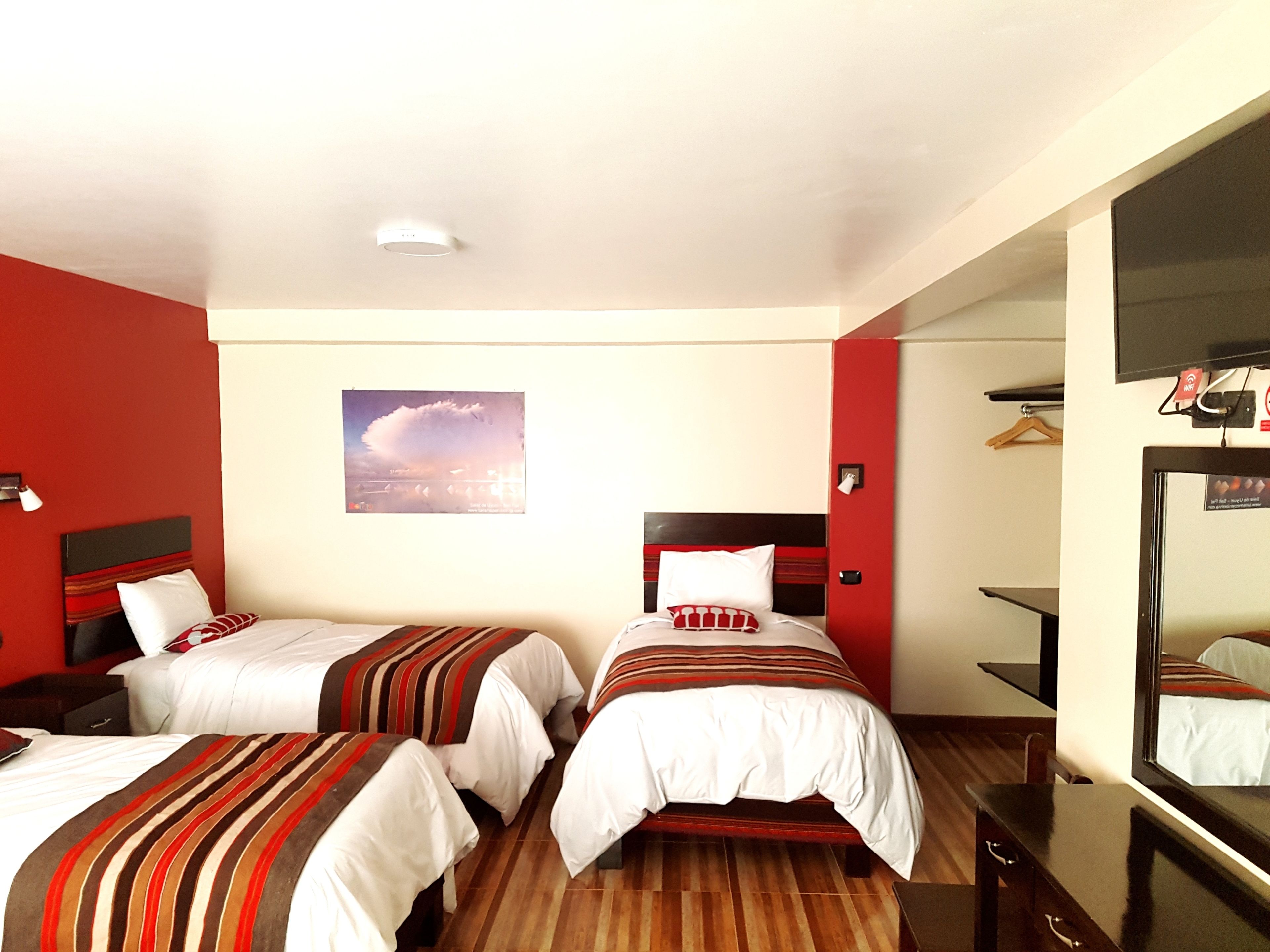 Habitación de hotel con dos camas, piso de madera, un espejo grande y una pintura de paisaje urbano en la pared.