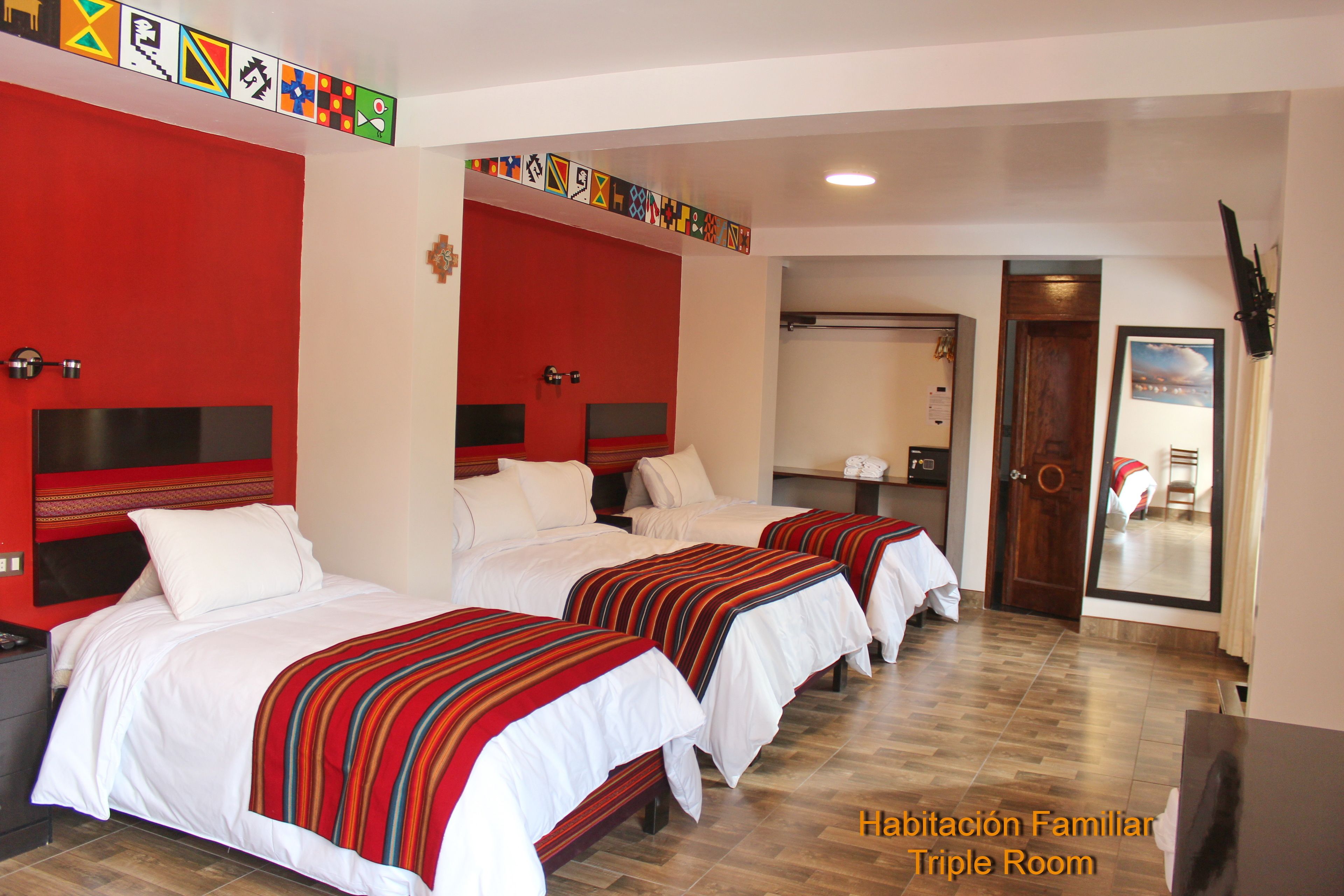 Habitación triple con tres camas, cada una con colcha a rayas rojas, almohadas blancas y cabeceros contra una pared roja.