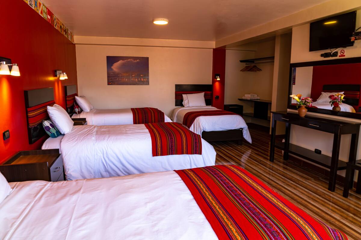 A hotel room with three beds, a desk, and a TV.