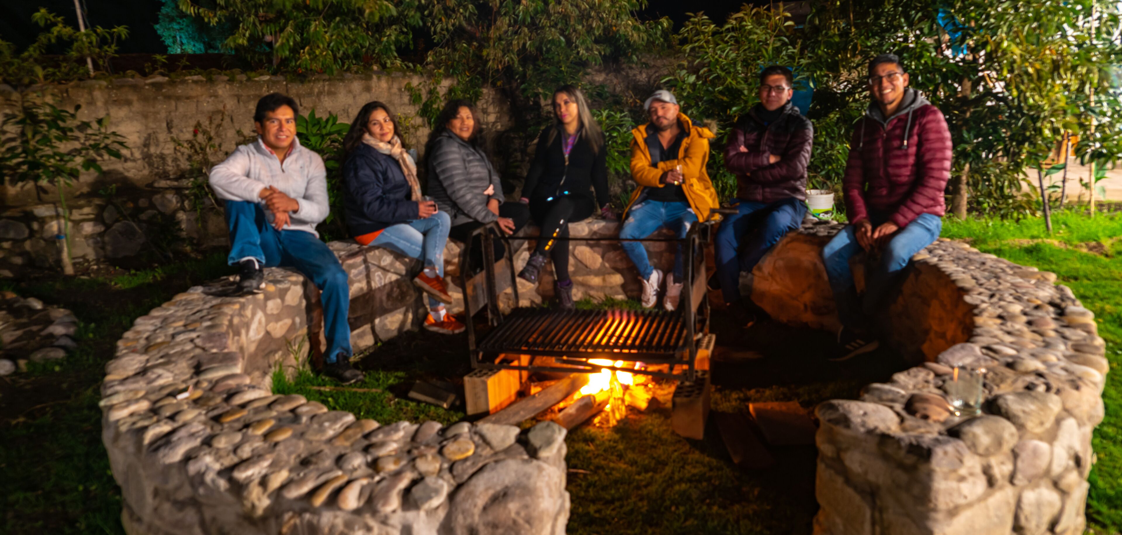 A group of people sitting around a stone fire pit at night.