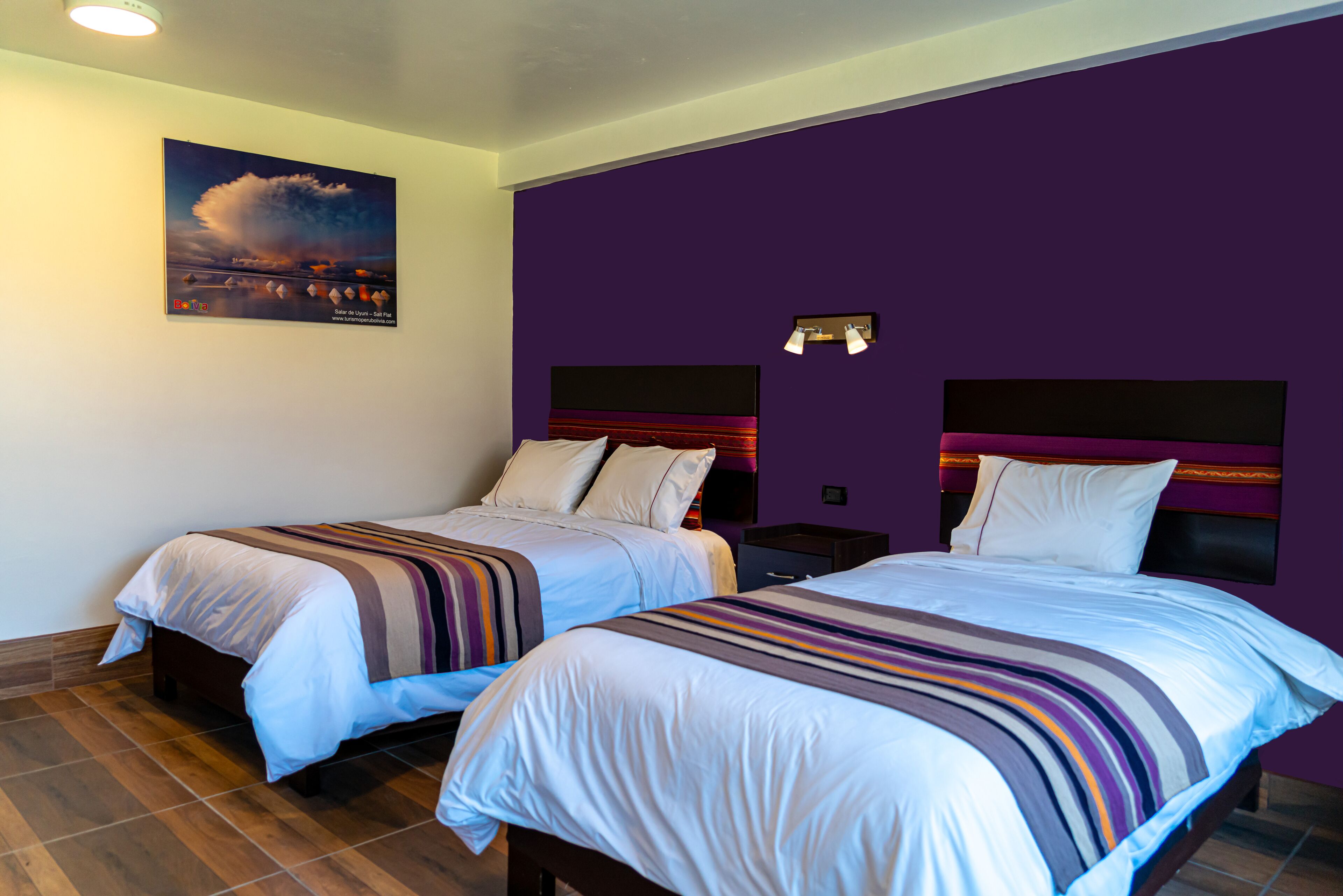 A hotel room with two beds, each with a striped blanket, a headboard with a black panel, and a wall-mounted light fixture.