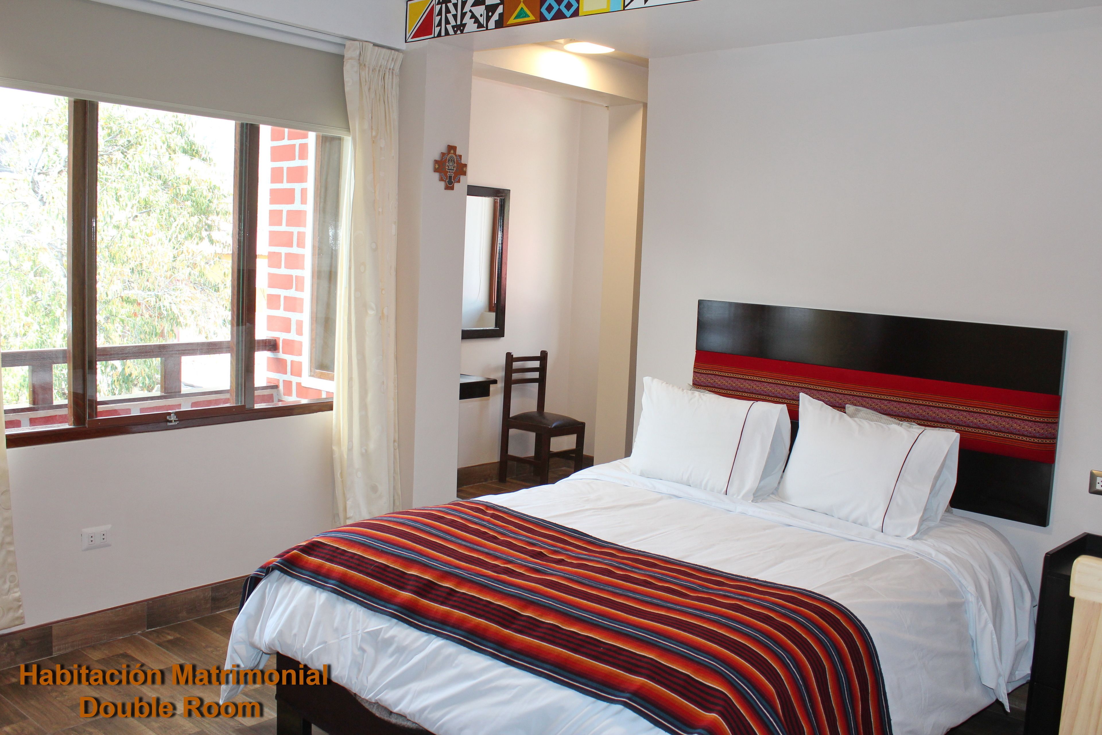 Una habitación doble con cama, una silla, ventana y puerta.