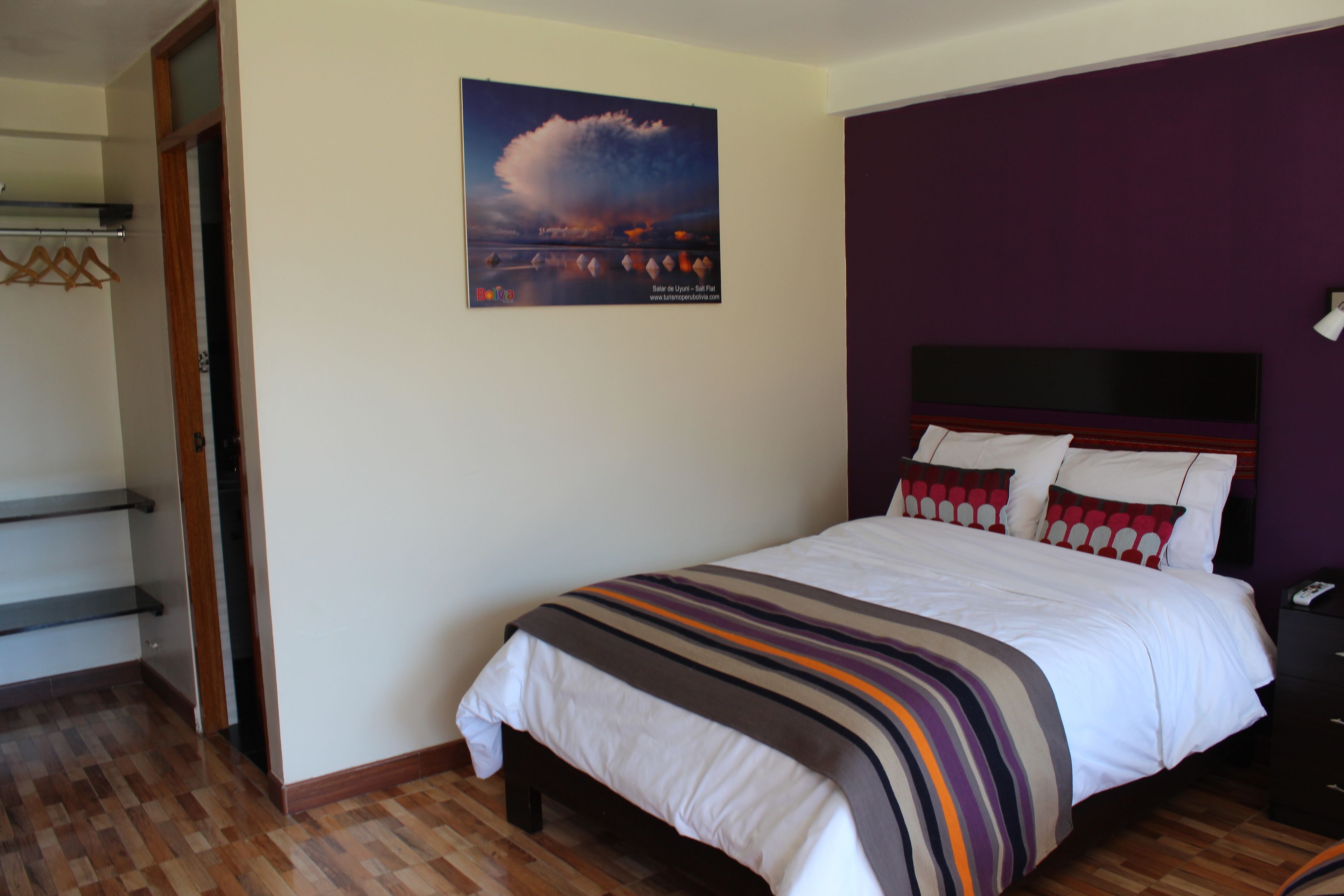 Un dormitorio con una cama, una mesita de noche, suelo de madera, una ventana y una puerta.