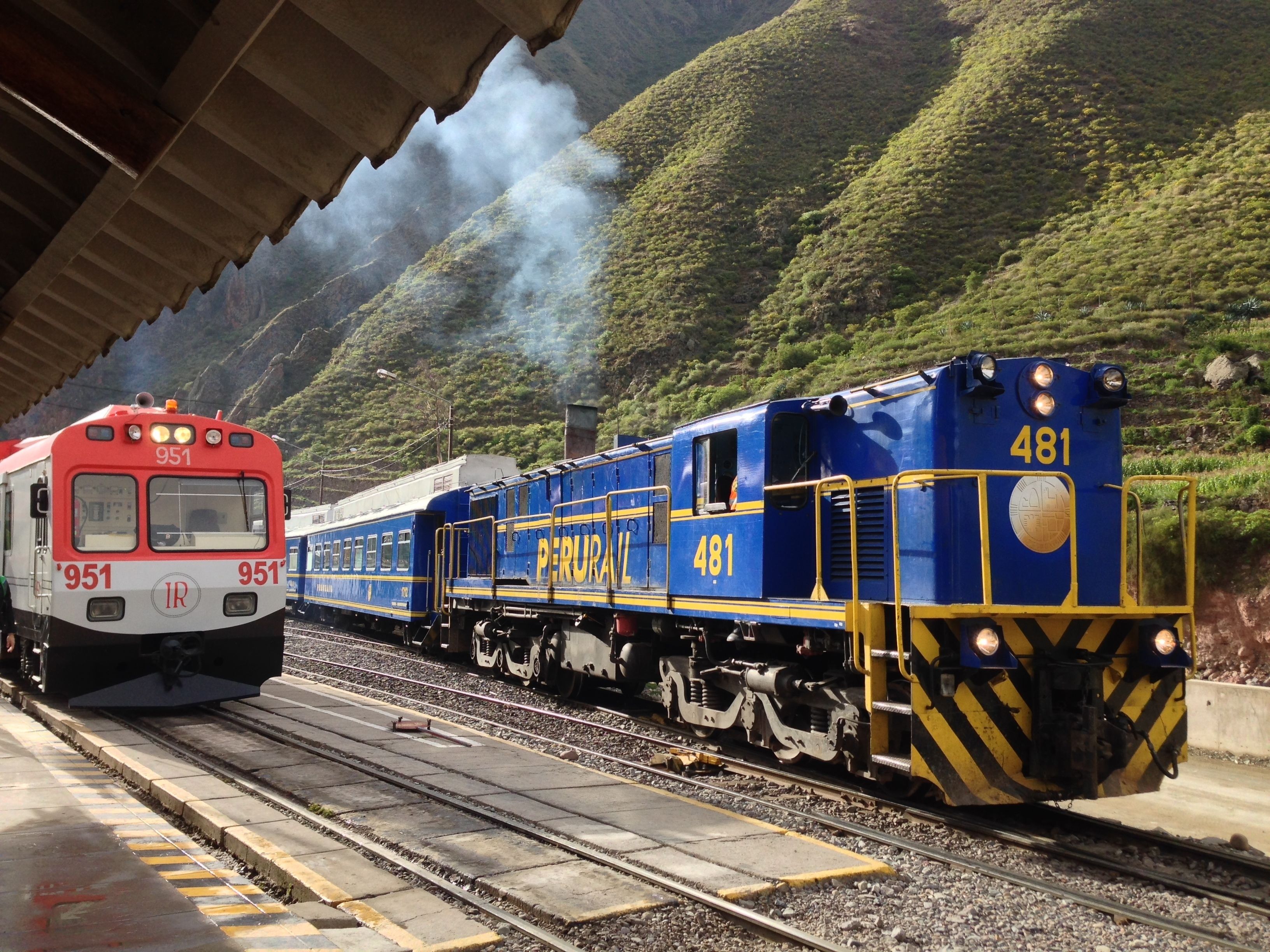 Una andana d'estació de tren amb dos trens, un vermell i un blau, on es pot veure el número 481 al tren blau.