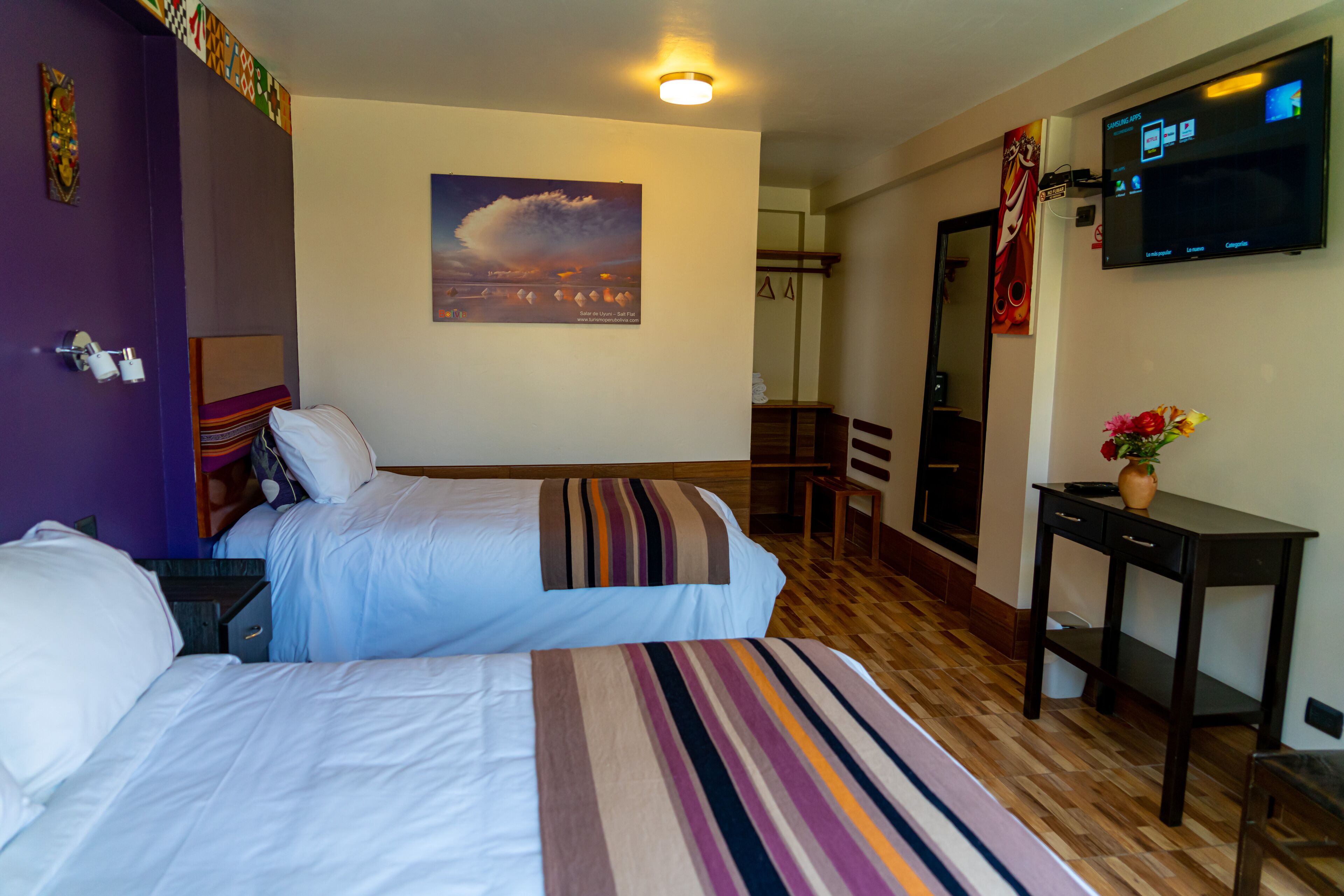 Habitación de hotel con dos camas, televisor, escritorio y un cuadro en la pared.