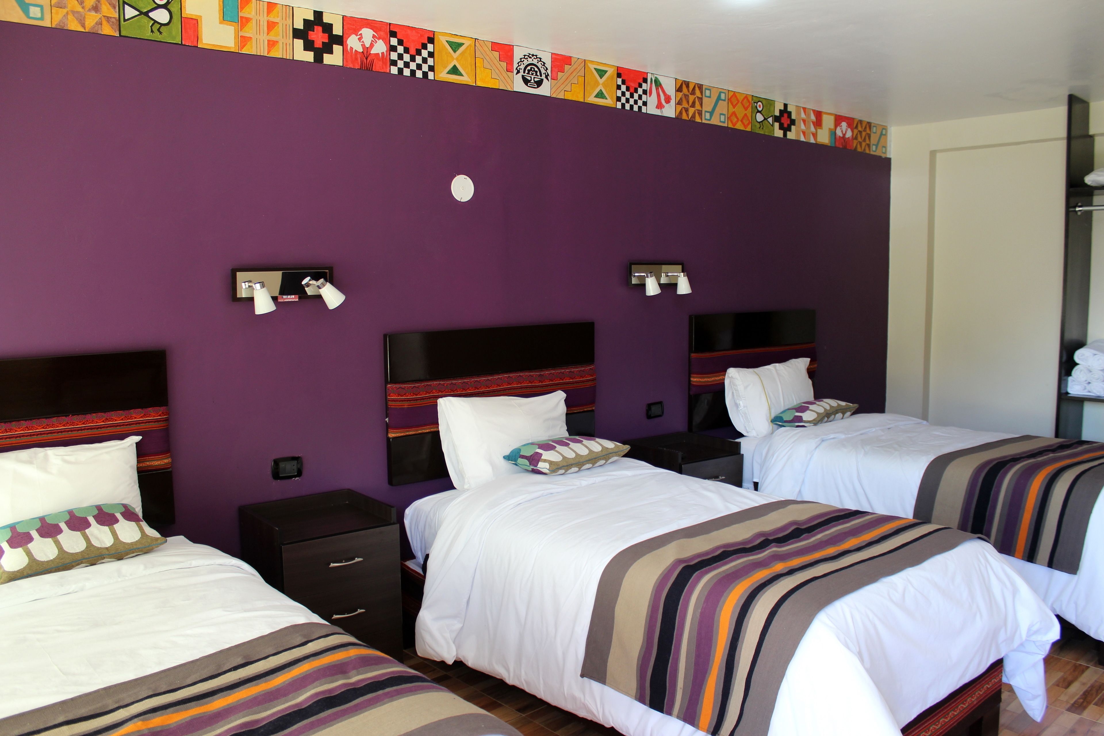 A hotel room with three beds, purple walls, and a colorful geometric border.