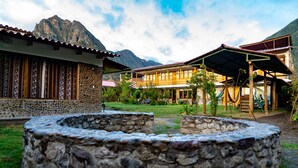 Edificio de paredes de piedra con balcón de madera, un hogar de piedra y una montaña al fondo.