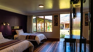 Habitación de hotel con dos camas, piso de madera, mesa de comedor y vistas a una montaña y una zona de estar al aire libre.