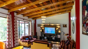 Sala de estar con techo de madera, un televisor de pantalla plana grande y un conjunto de sofás.