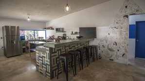 A modern kitchen with a central island, bar stools, and a decorative wall mural. - Todos Santos Hostel (Todos Santos)