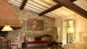 Ein rustikaler Raum mit sichtbaren Holzbalken, einer Steinwand, einem roten Sofa, einem weißen Sofa und einem gemusterten Teppich.