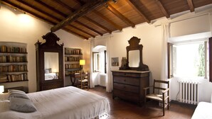 Ein Schlafzimmer mit einem großen Bett, Holzmöbeln, einem Bücherregal und einem Fenster mit Vorhängen.