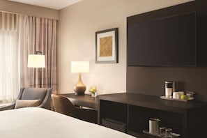 Habitación de hotel con cama, escritorio con lámpara, una silla, televisor y cafetera.