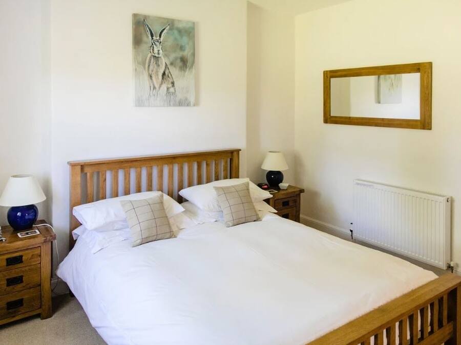 A neatly made bed with white linens, two bedside tables with lamps, a wooden headboard, a wall-mounted mirror, and a radiator.