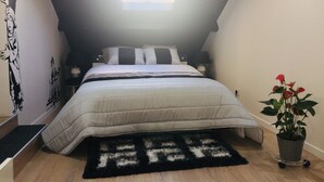 Une chambre à coucher avec un lit, une fenêtre, un mur décoré d’œuvres d’art, une plante et un tapis.