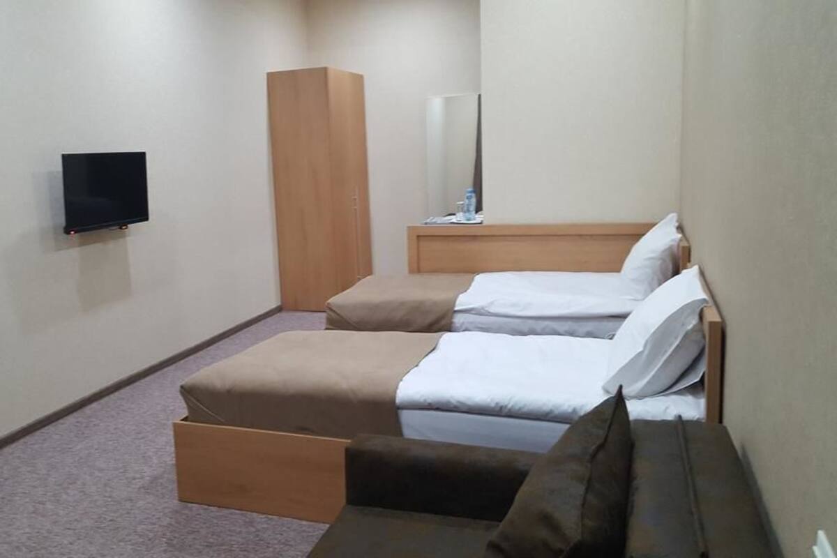 A small, single-room hotel room with a bed, a TV, a wardrobe, and a mirror.