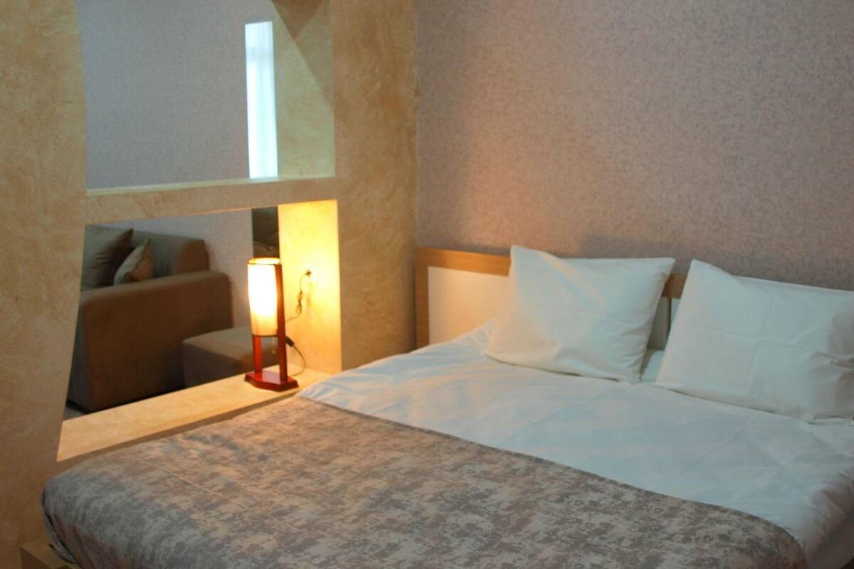 A hotel room with a bed, a nightstand, a lamp, a sofa, and a window.