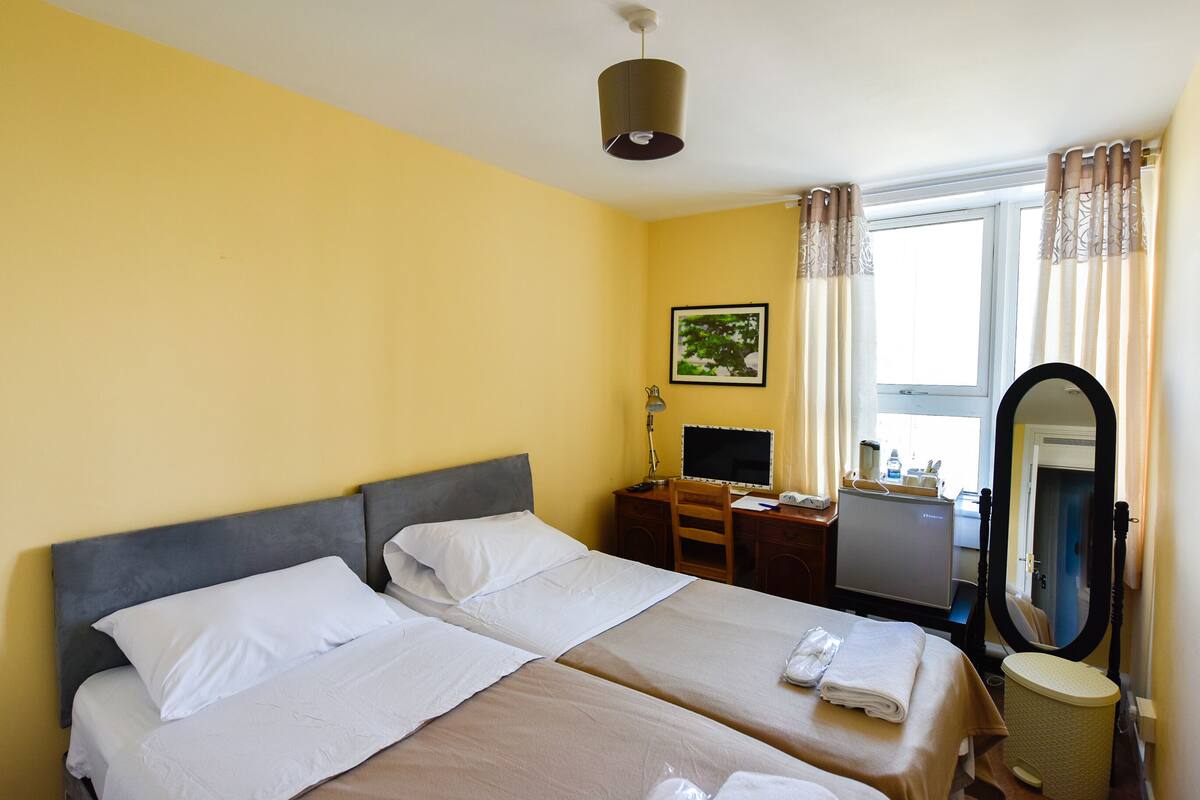 Une chambre d’hôtel avec deux lits, un bureau, un ordinateur, un miroir et une fenêtre avec des rideaux.