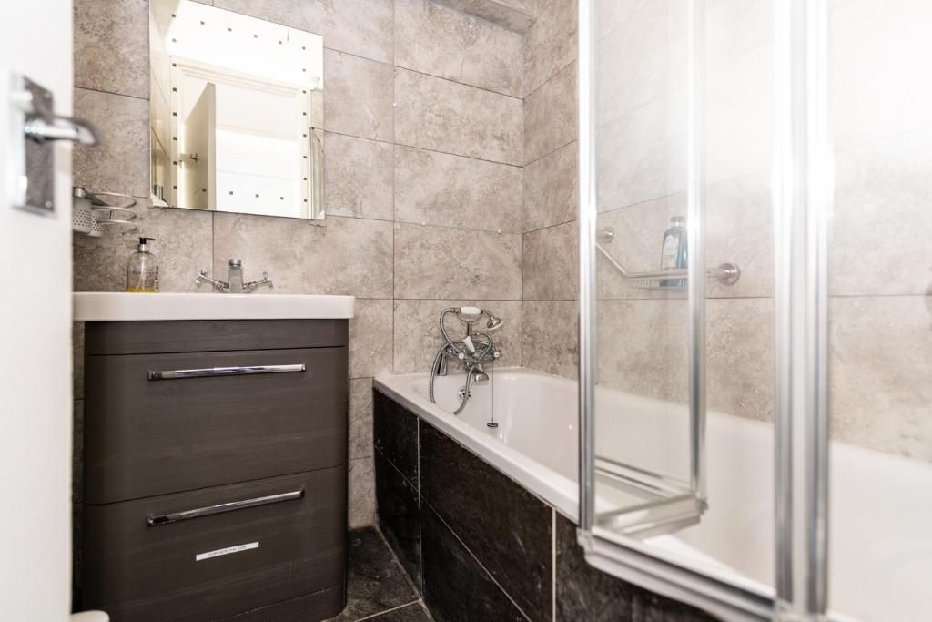A bathroom with a dark wooden vanity, a white bathtub, and a glass shower enclosure.