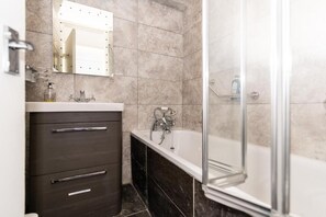 A bathroom with a dark wooden vanity, a white bathtub, and a glass shower enclosure. - Bray Apartment (London)