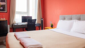 Une chambre d’hôtel avec un lit, un bureau, une chaise et une fenêtre avec des rideaux.