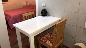 A small room with a white table and a wooden chair with a patterned cushion. There is a bed with a pink bedspread in the background. - 1 Ambiente Avenida Cordoba (Buenos Aires)