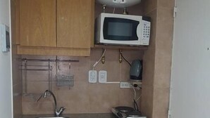 A compact kitchen with wooden cabinets, a microwave, a sink, and a small refrigerator. - 1 Ambiente en Recoleta (Buenos Aires)