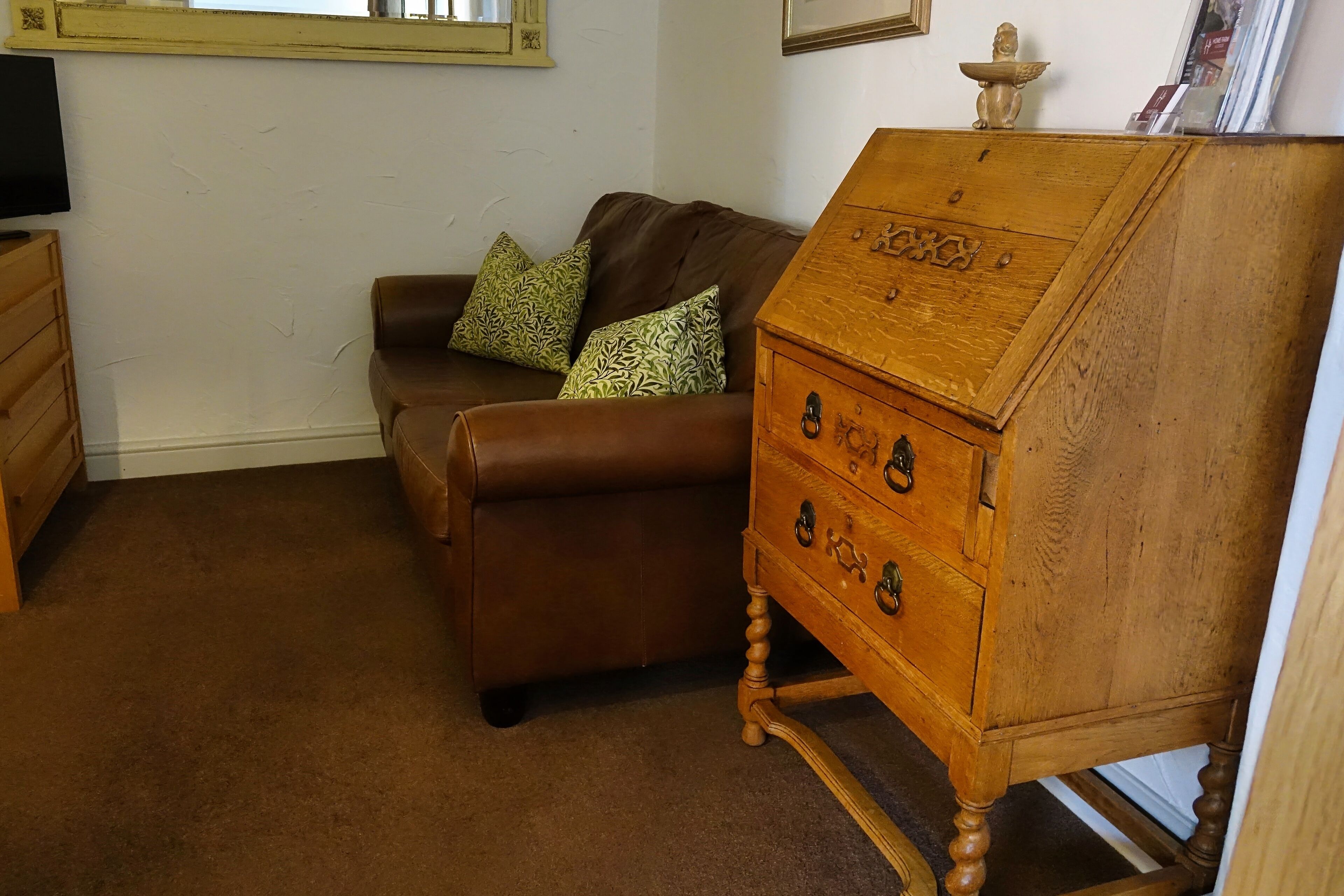 Een woonkamer met een bruine leren bank, twee decoratieve kussens met een patroon, een houten dressoir en een televisie op een houten meubel.