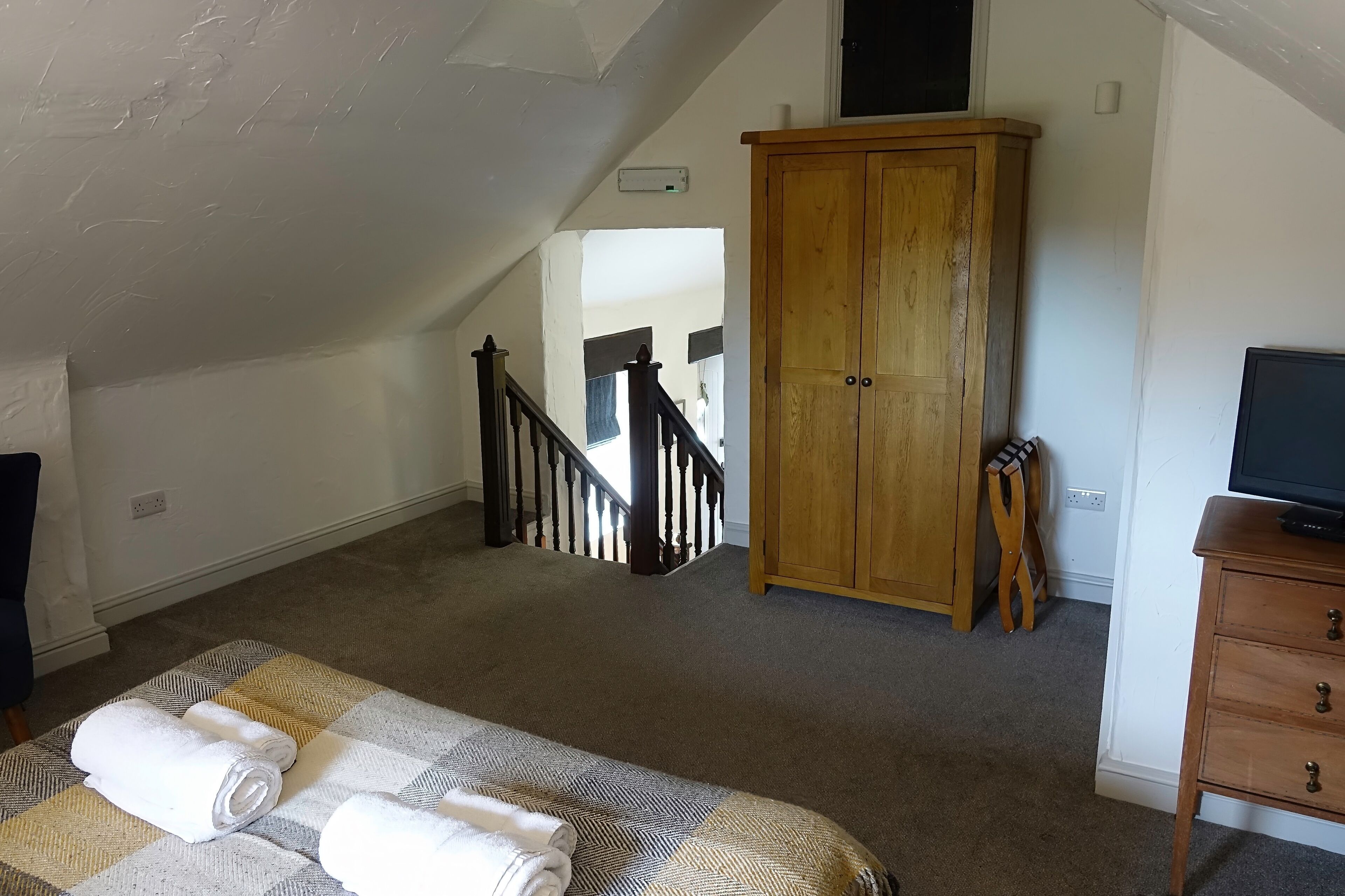 A bedroom with a bed, a wooden wardrobe, a television on a dresser, and a staircase leading to another room.
