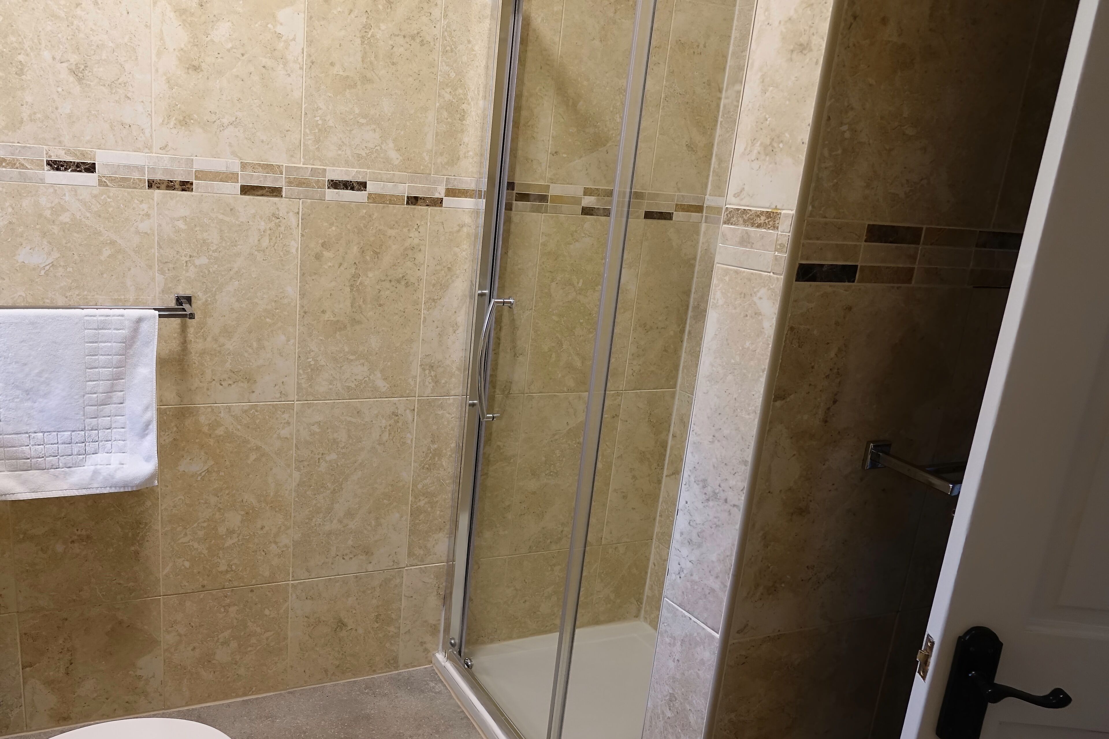 A bathroom with beige tiles, a glass shower enclosure, and a white towel hanging on a rack.