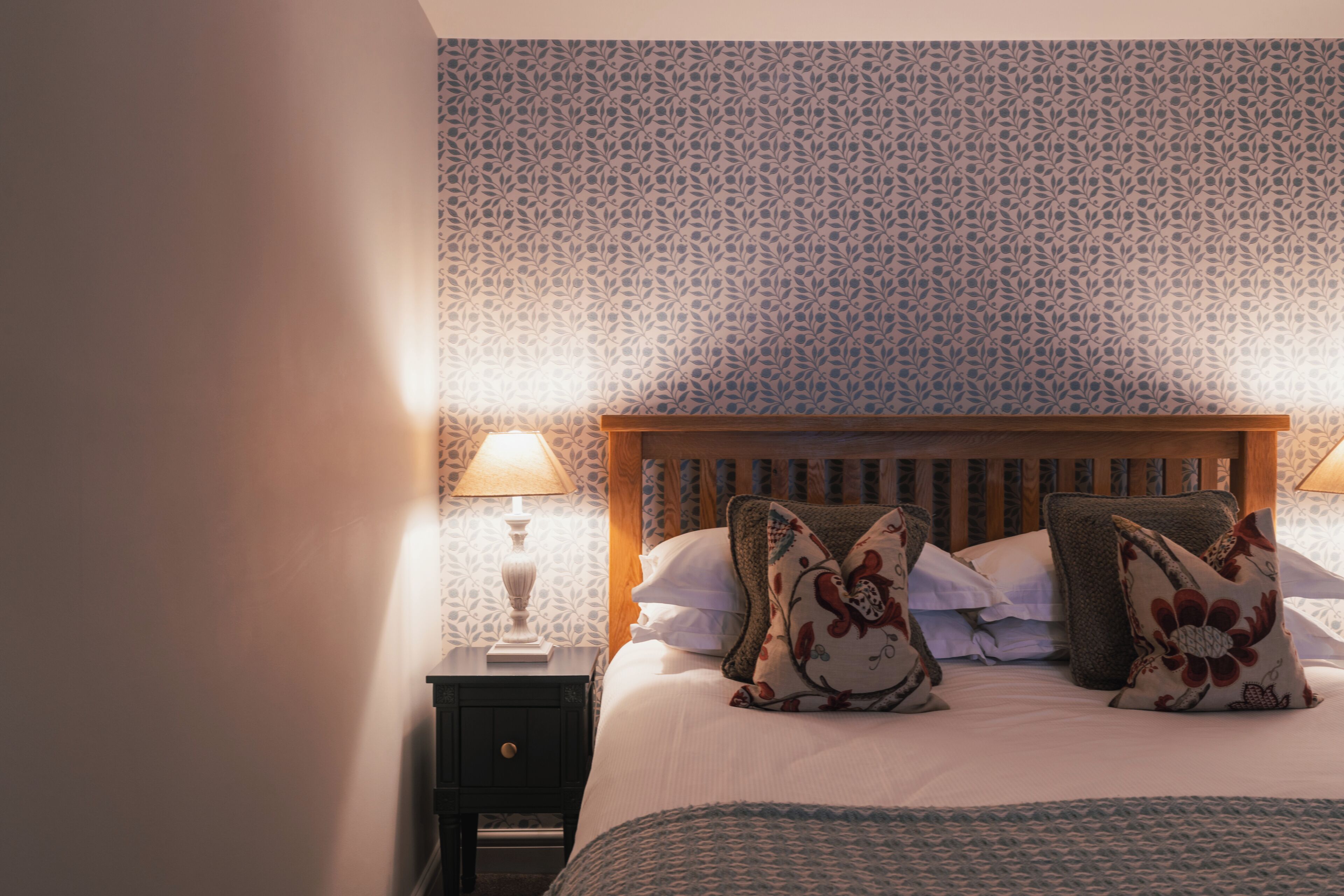 Un dormitorio con papel tapiz estampado, cabecera de madera y almohadas decorativas.