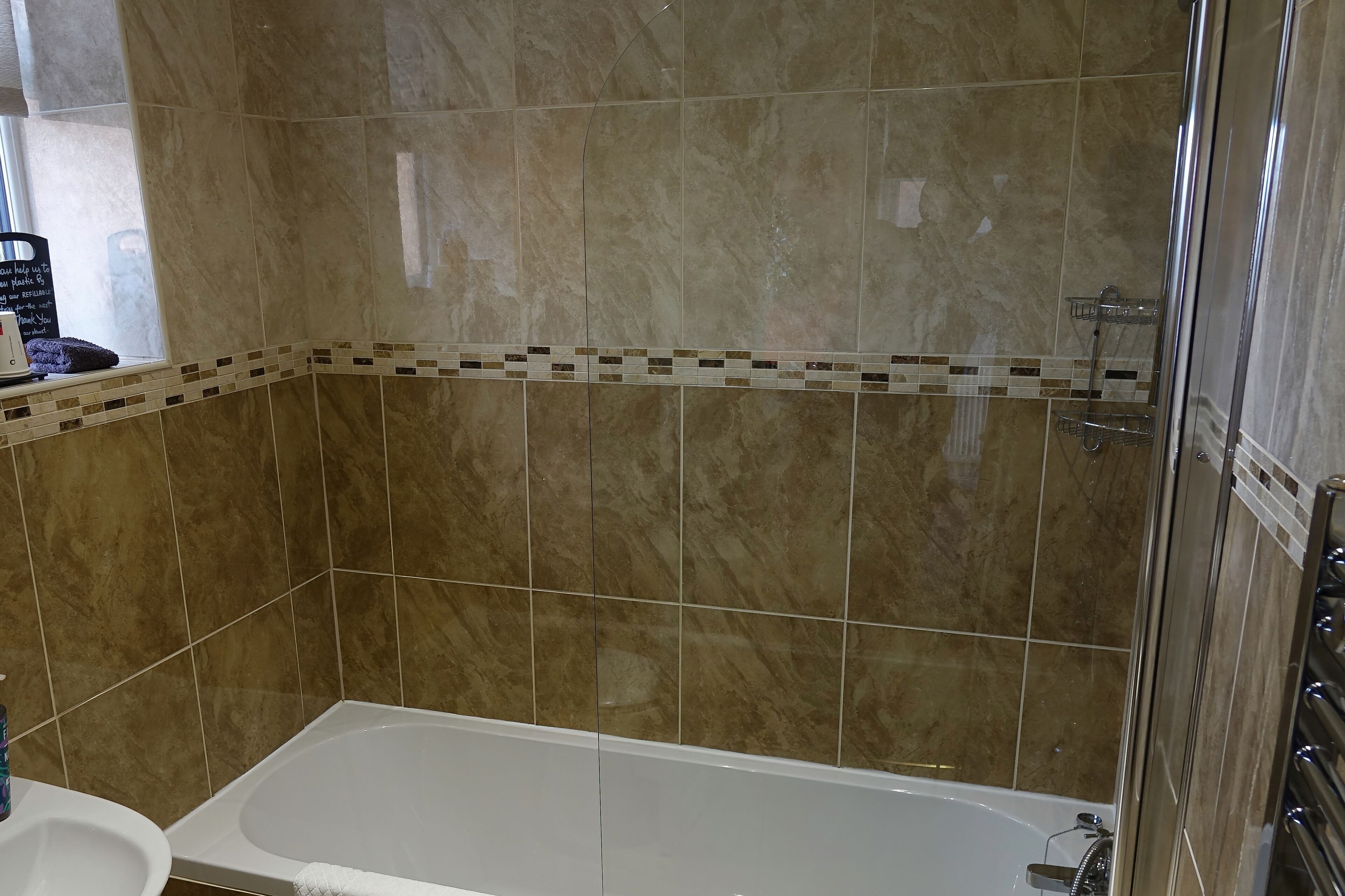 Un baño con bañera, ducha y pared de azulejos con detalle en mosaico.