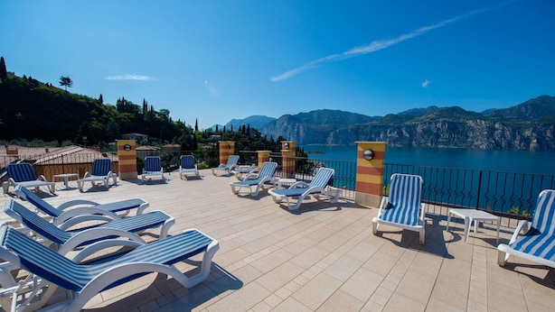 A terrace with sun loungers and a view of a lake and mountains. - Hotel Cristallo (Malcesine)