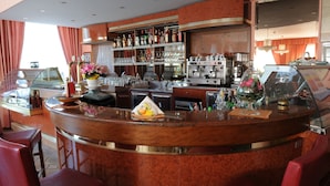 A bar area with a marble counter, bar stools, a coffee machine, and a variety of bottles and glasses on shelves. - Hotel Cristallo (Malcesine)