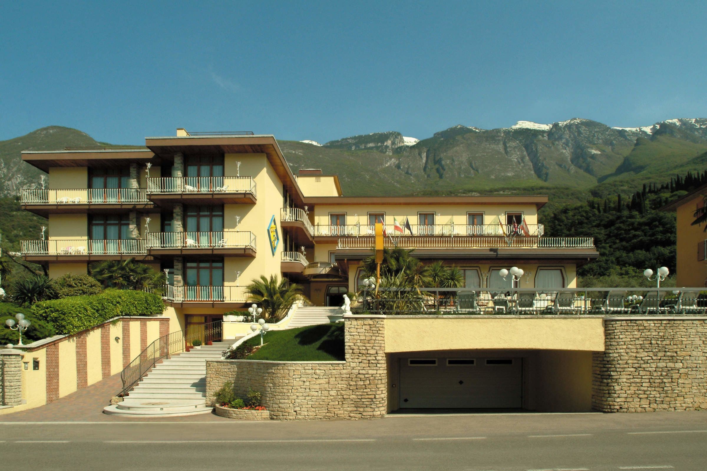 A multi-story hotel with balconies, a stone facade, and a mountain backdrop.