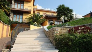 A hotel entrance with a stone staircase leading up to a building with balconies. - Hotel Cristallo (Malcesine)
