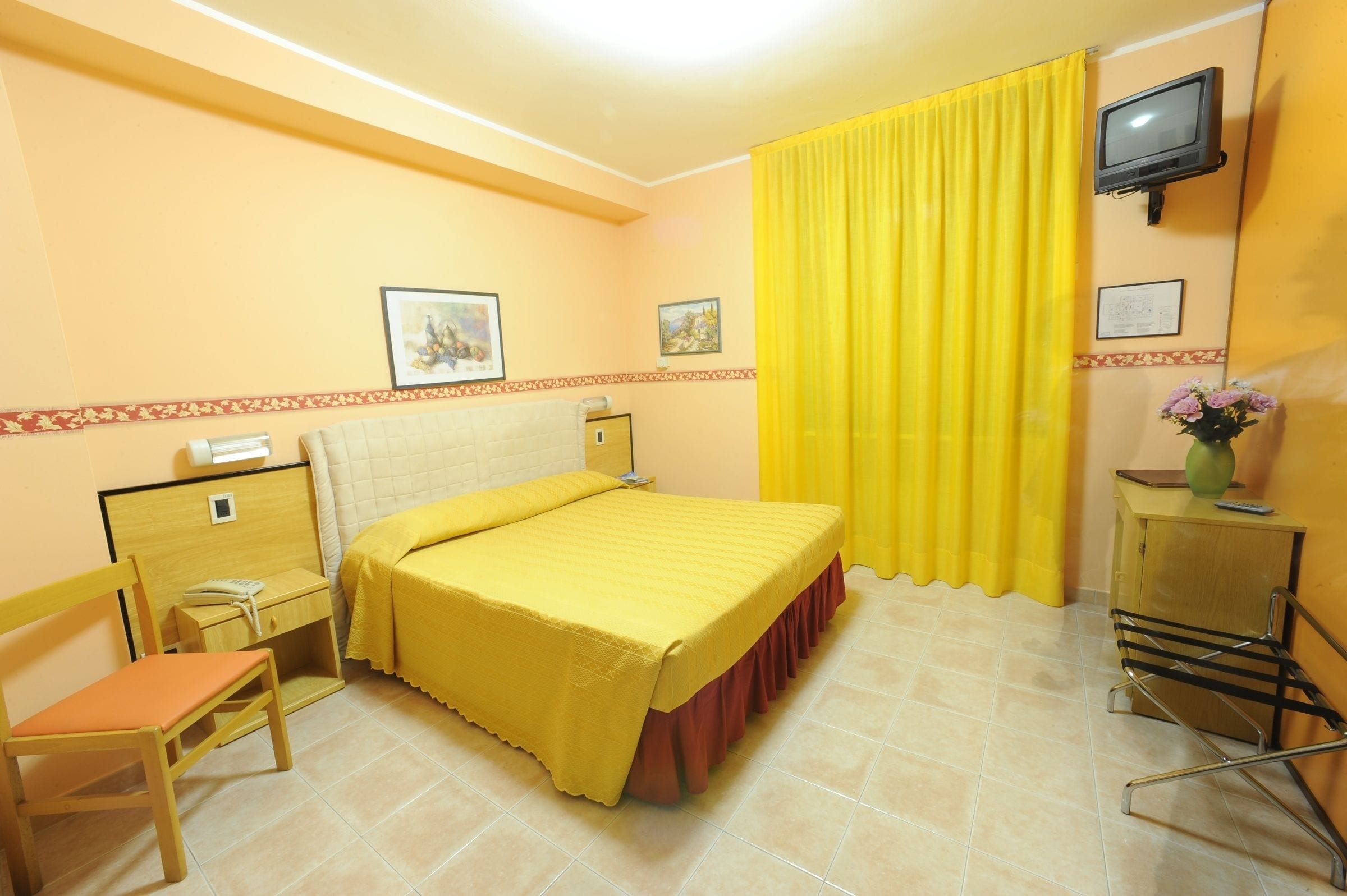 Una habitación de hotel con cama, escritorio, silla, televisor y cortina.