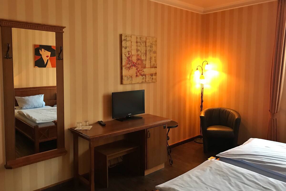 Habitación de hotel con cama, escritorio con computadora, una silla, lámpara y un cuadro en la pared.