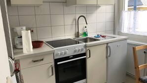 Pieni, käytännöllinen keittiö, jossa on valkoiset kaapit, liesi, uuni ja pesuallas.