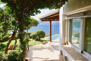 A balcony with a view of the sea, a pergola, and a stone pathway leading to a pool.