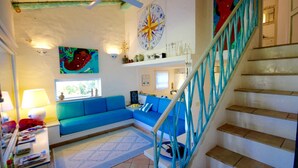 Ein Wohnzimmer mit blauem Sofa, einer Treppe mit blauen Geländern und einem dekorativen Wandbild.