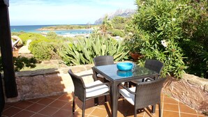 A patio with a table and chairs, overlooking a coastal landscape with vegetation and a view of the sea. - Villa Sara (Olbia)