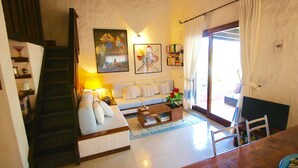 A living room with a sofa, coffee table, and a staircase. There are bookshelves and a painting on the wall. - Villa Sara (Olbia)