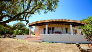 A covered outdoor seating area with a pergola, steps leading up to it, and a view of a building in the background. - Villa Twin (Golfo Aranci)