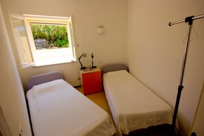 Ein kleines, kompaktes Zimmer mit zwei Einzelbetten, einem Schreibtisch mit Lampe und einem Fenster mit Blick auf Grünflächen.