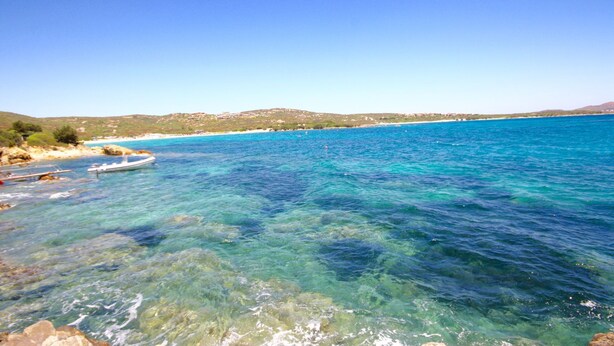 A coastal scene with clear turquoise water, rocky shore, and distant hills. - Villa Twin (Golfo Aranci)
