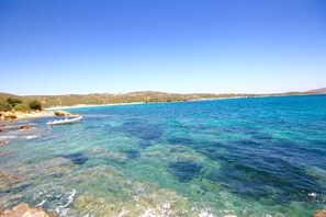 Paisaje costero con agua turquesa cristalina, costa rocosa y colinas distantes.