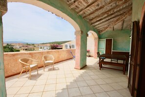 A terrace with wicker chairs, a wooden table, and a view of the surrounding area. - Casa Gabriella (Olbia)