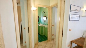 Un couloir avec un sol carrelé de carreaux verts, un lavabo et un miroir au fond.